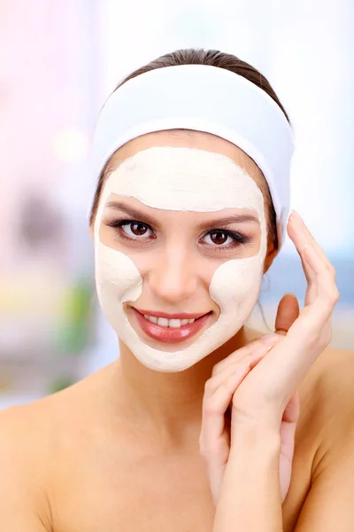 Jeune femme avec masque facial en argile, sur fond lumineux — Photo