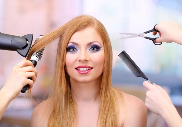 Beautiful woman and hands with brushes, scissors and hairdryer in beauty salon — Stock Photo, Image