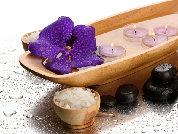 Spa stones and wooden bowl with candles and purple flower, on wet background — Stock Photo, Image