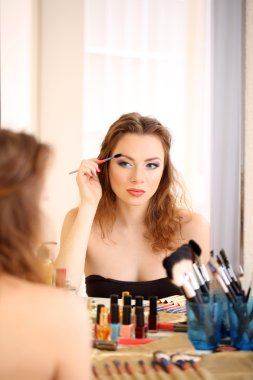 Genç ve güzel bir kadın aynanın yanında makyaj yapıyor.