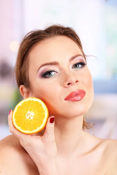 Beautiful young woman with bright make-up, holding orange, on bright background — Stock Photo, Image