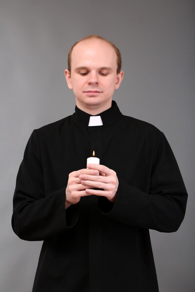 Portrait of young Pastor holding candle in his hand,on gray background