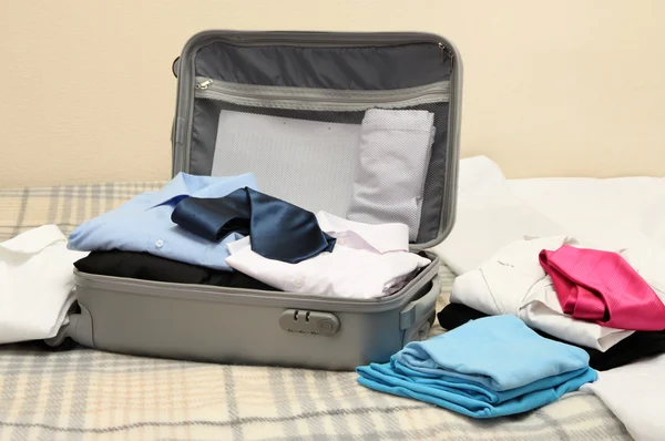 Open grey suitcase with clothing on bed — Stock Photo, Image