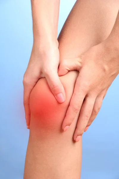 Mujer sosteniendo dolor de rodilla, sobre fondo azul — Foto de Stock