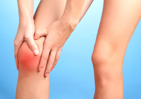 Žena držící bolavé koleno, na modrém pozadí — Stock fotografie