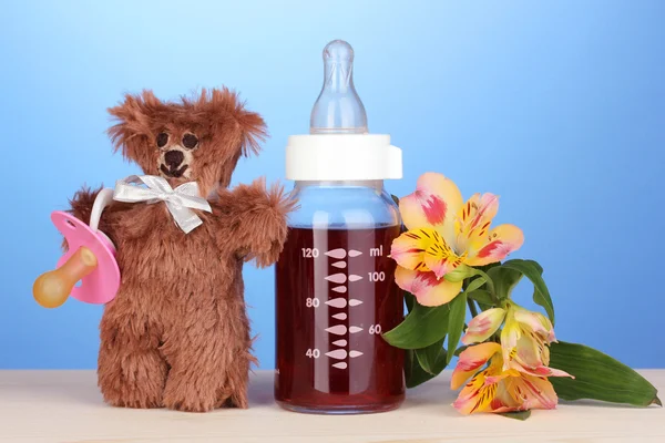 Baby bottle with fresh juice and teddy bear on blue background — Stock Photo, Image