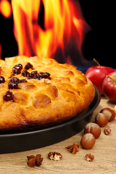 Gustosa torta fatta in casa con marmellata, su tavolo di legno su sfondo fiamma — Foto Stock