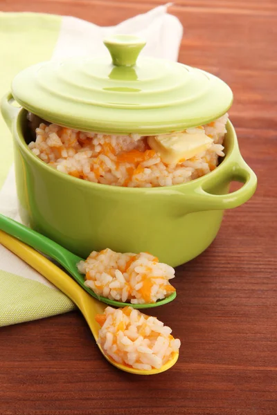 Taste rice porridge with pumpkin in saucepan on wooden background — Stock Photo, Image