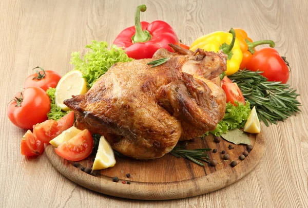 Hela rostad kyckling med grönsaker på tallriken, på träbord — Stockfoto