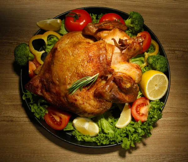 Whole roasted chicken with vegetables on plate, on wooden table — Stock Photo, Image