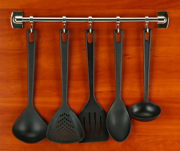 Black kitchen utensils on silver hooks, on wooden background — Stock Photo, Image