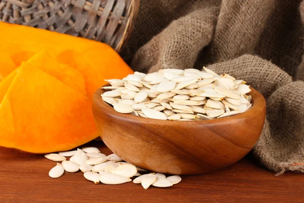 Pumpkin seeds in wooden bowl, on sackcloth background — Stock Photo, Image