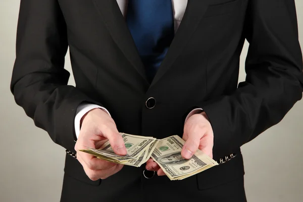Obchodní muž počítá peníze na šedém pozadí — Stock fotografie