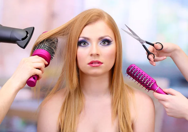 Beautiful woman and hands with brushes, scissors and hairdryer in beauty salon — Stock Photo, Image