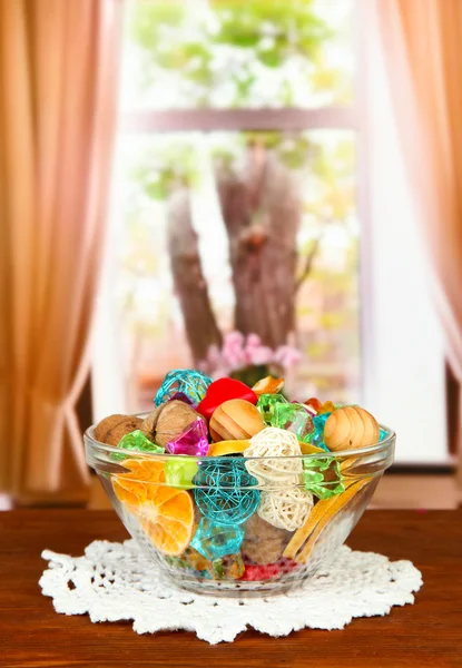 Dried oranges, wicker balls and other home decorations in glass bowl, on bright background — Stock Photo, Image