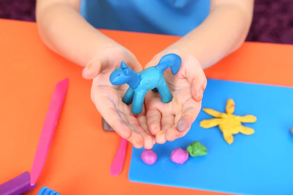 Child's hands holding hand-made plasticine hourse over desk — Stock Photo, Image