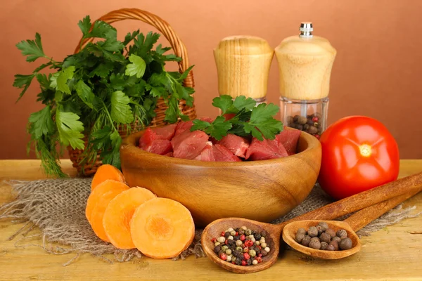Rohes Rindfleisch mit Kräutern und Gewürzen auf Holztisch auf braunem Hintergrund — Stockfoto