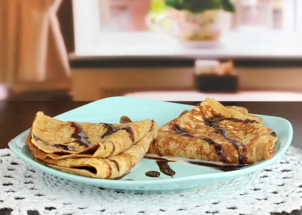 Söta pannkakor på tallrik med kondenserad mjölk på bordet i rummet — Stockfoto