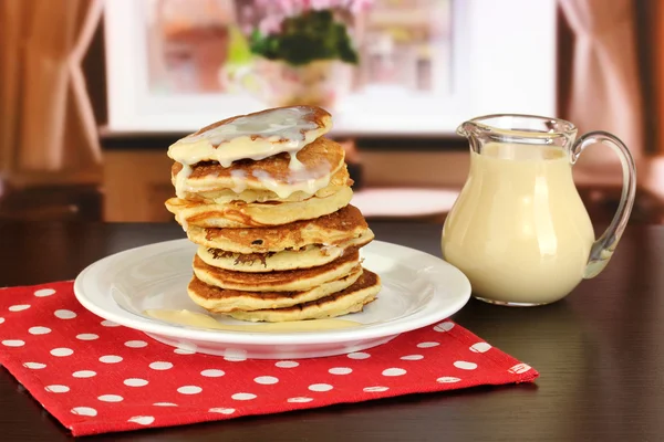 Zoete pannenkoeken op plaat met gecondenseerde melk op tafel op kamer — Stockfoto