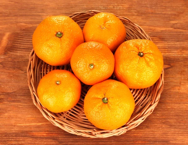 Mandarinas saborosas no tapete de vime no fundo de madeira — Fotografia de Stock