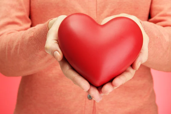 Corazón rojo en manos de mujer, sobre fondo rojo — Foto de Stock