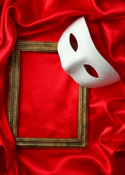 White mask and empty frame on red silk fabric — Stock Photo, Image