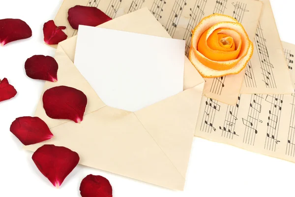 Alter Umschlag mit leerem Papier und getrockneten Rosenblättern auf Notenblättern in Nahaufnahme — Stockfoto