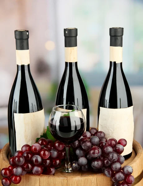 Состав винных бутылок, бокалов и винограда, на деревянном бочке, на ярком фоне — стоковое фото