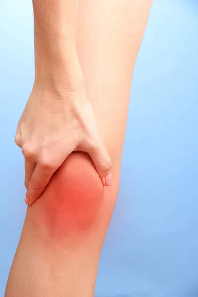 Mujer sosteniendo dolor de rodilla, sobre fondo azul — Foto de Stock