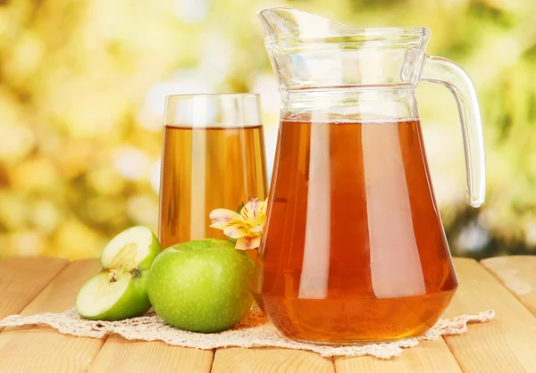 Vol glas en kruik van appelsap en appels op houten tafel buiten — Stockfoto