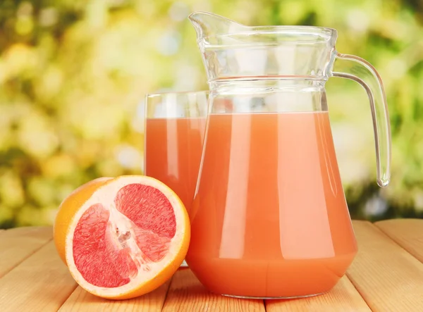 Vol glas en kruik van grapefruitsap en grapefruits op houten tafel buiten — Stockfoto