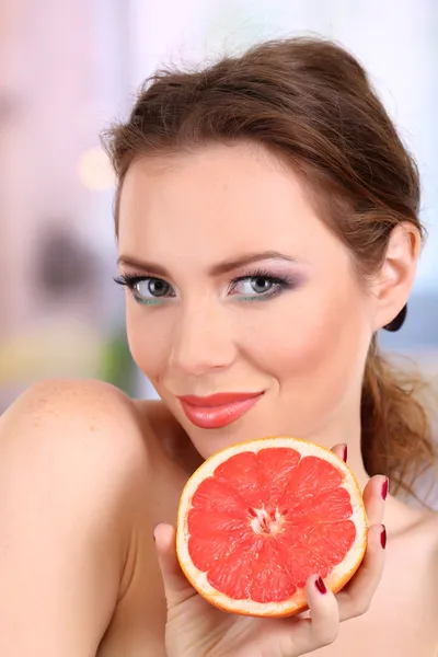 Beautiful young woman with bright make-up, holding grapefruit, on bright background — Stock Photo, Image