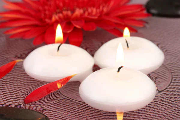 Piedras de spa con flores y velas en agua en el plato —  Fotos de Stock