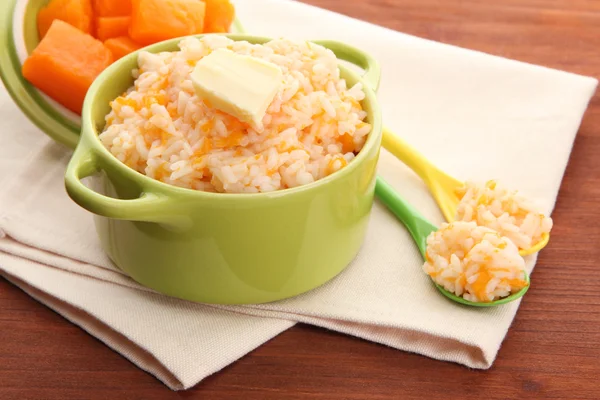 Taste rice porridge with pumpkin in saucepans on wooden background — Stock Photo, Image