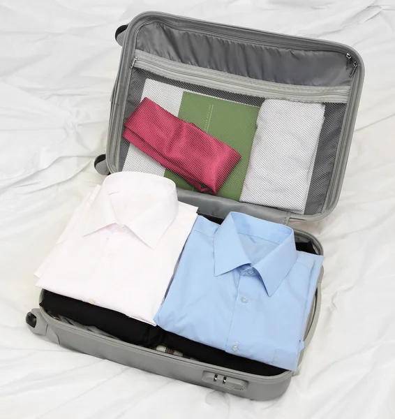 Ανοικτό γκρι βαλίτσα με ενδυμασία σε κρεβάτι — Φωτογραφία Αρχείου