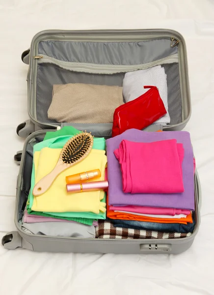 Open grey suitcase with clothing on bed — Stock Photo, Image