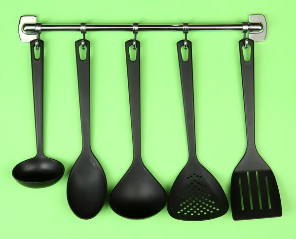 Black kitchen utensils on silver hooks, on green background — Stock Photo, Image