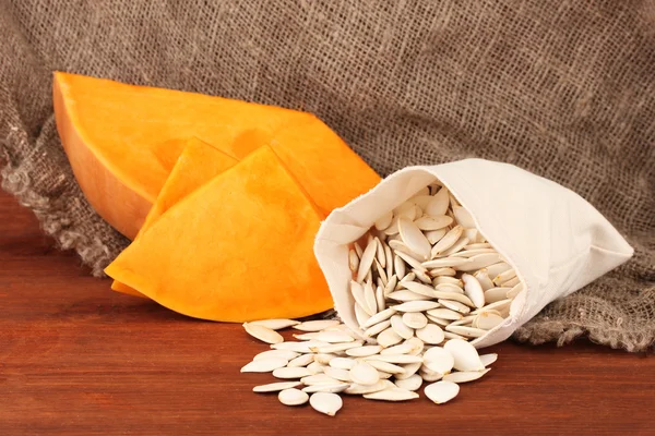 Pumpkin seeds in sack, on wooden background — Stock Photo, Image