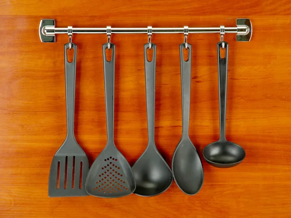 Black kitchen utensils on silver hooks, on wooden background — Stock Photo, Image