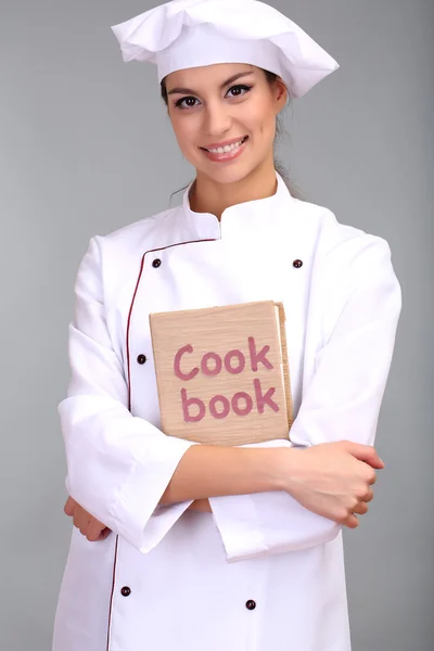 요리 책에 회색 배경으로 젊은 여자 요리사의 초상화 — 스톡 사진