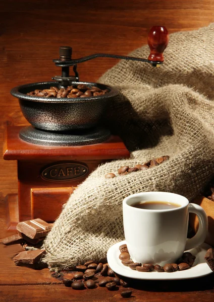 Koffiemolen en kop koffie op bruine houten ondergrond — Stockfoto