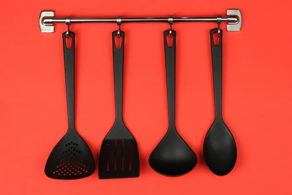 Black kitchen utensils on silver hooks, on red background — Stock Photo, Image