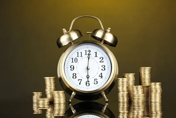 Relógio despertador com moedas em fundo escuro — Fotografia de Stock