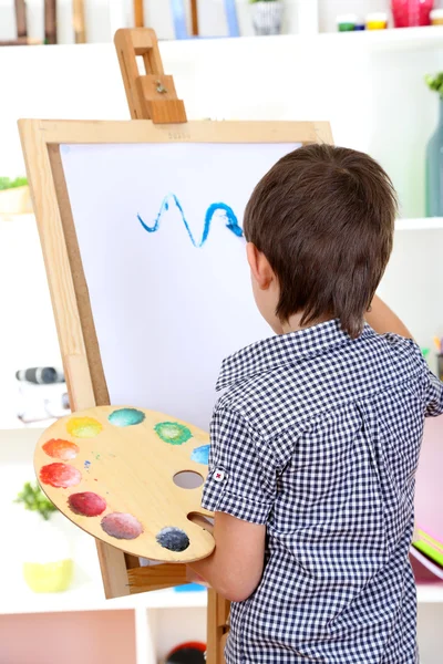 Little boy painting paints picture on easel — Stock Photo, Image