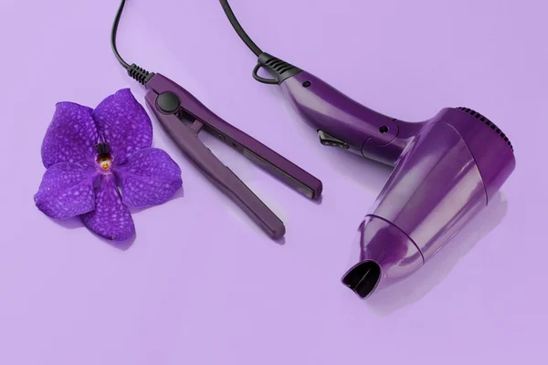 Hair dryer and straighteners on purple background — Stock Photo, Image