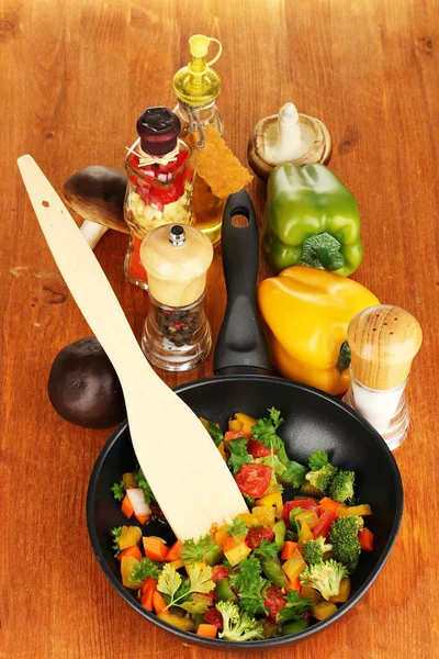 Hortalizas frescas en rodajas en sartén con especias e ingredientes sobre mesa de madera — Foto de Stock