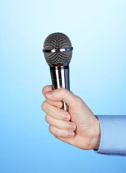 Male hand with microphone on blue background — Stock Photo, Image