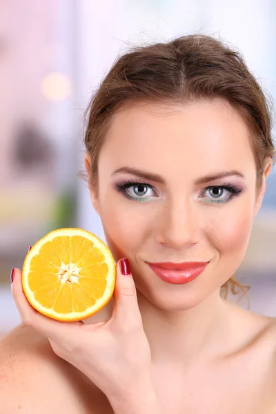 Hermosa joven con maquillaje brillante, sosteniendo naranja, sobre fondo brillante —  Fotos de Stock