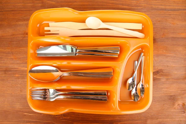 Πορτοκαλί πλαστικά μαχαιροπήρουνα δίσκο με ελεγμένη μαχαιροπήρουνα και ξύλινα κουτάλια στο ξύλινο τραπέζι — Φωτογραφία Αρχείου