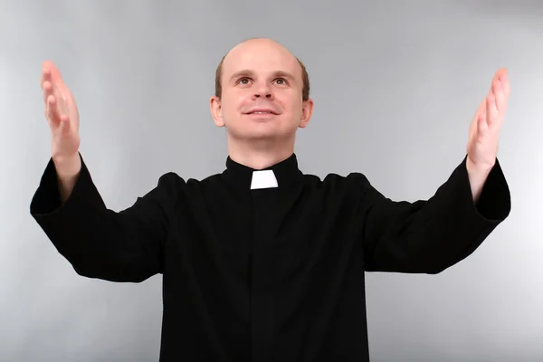 Joven sacerdote sobre fondo gris — Foto de Stock